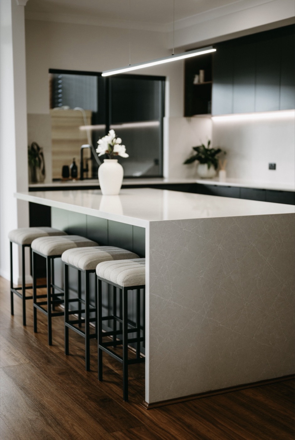 A stone waterfall-island kitchen with linen bar stools and warm timber floors.