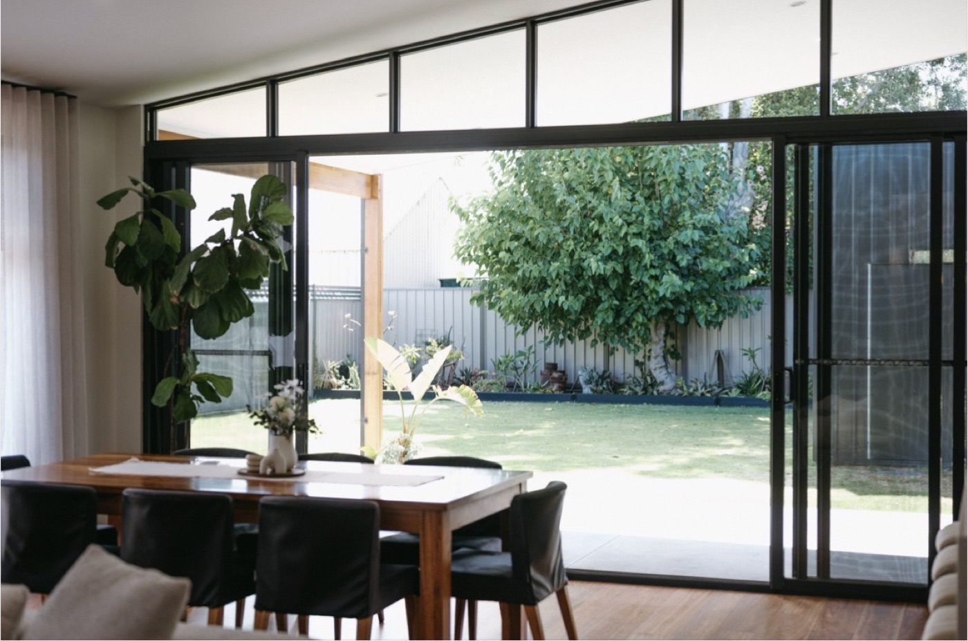 A dining room opening to the garden through black steel-framed doors.